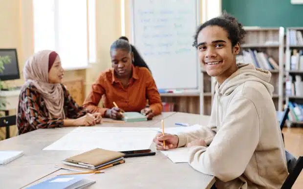 Three people sitting at a table with pens and paper