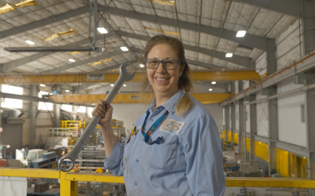 Woman in work clothes and protective glasses holding a wrench in a warehouse