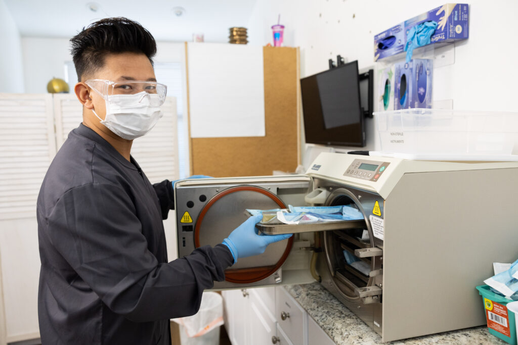 A person in protective clothing sterilizes dental instruments.