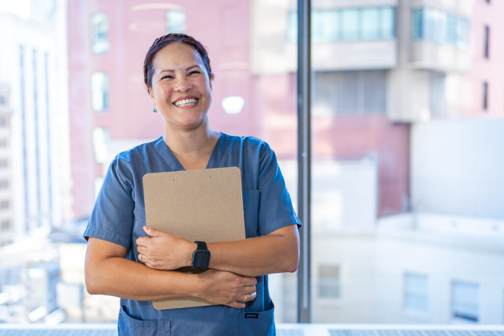 Woman wearing medical scrubs and holding a clipboard, smiling