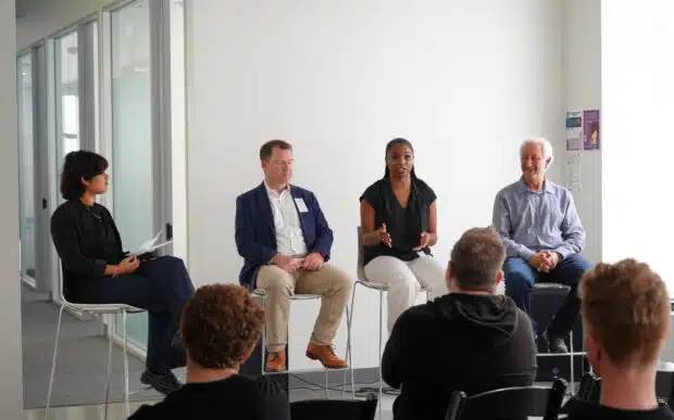 Four people sitting in front of a crowd during a panel discussion