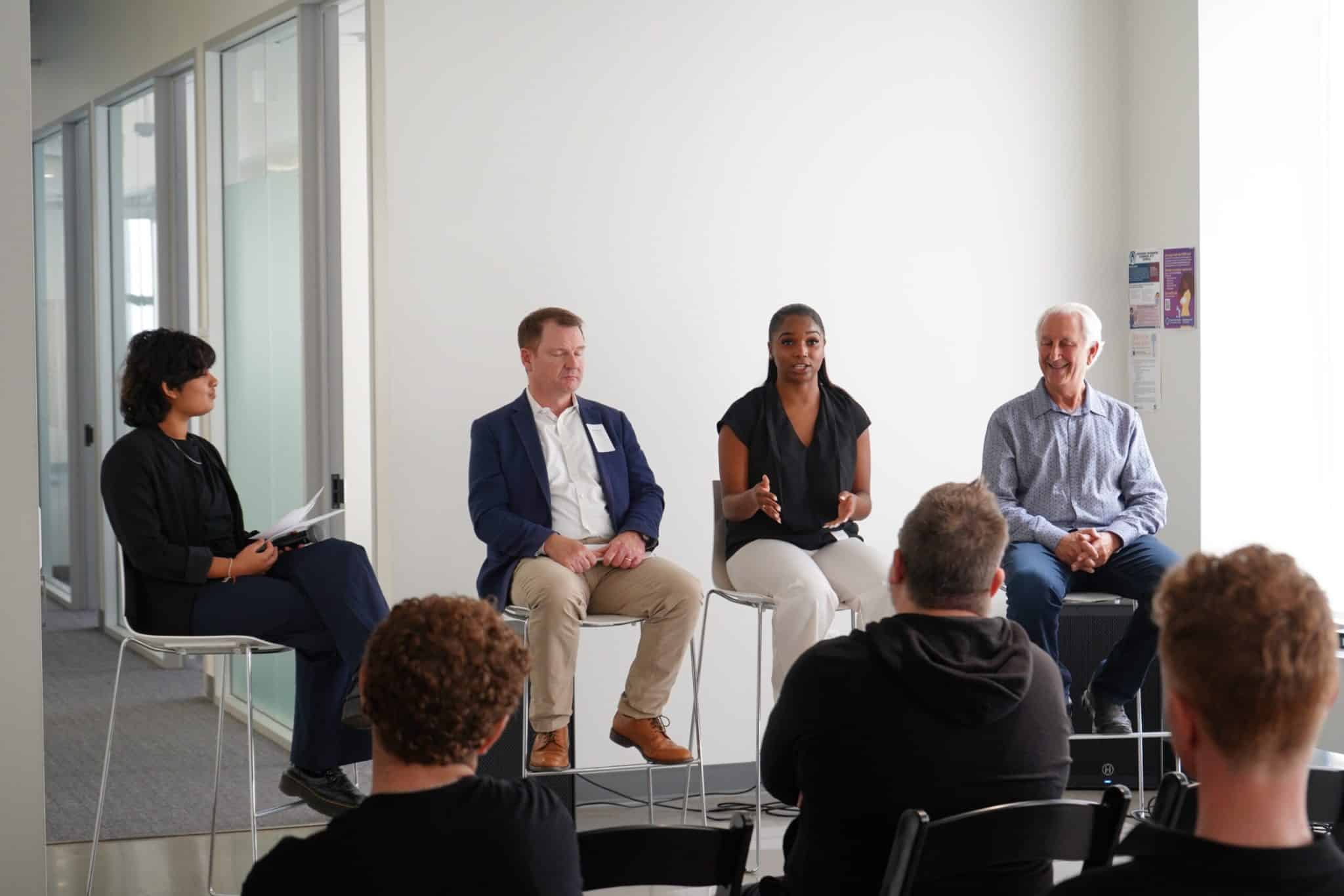 Four people sitting in front of a crowd during a panel discussion